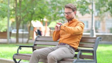 Genç adam dışarıda oturuyor ve Smartwatch kullanıyor.