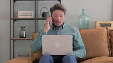 Orta yaşlı adam telefonda dizüstü bilgisayarla konuşuyor.