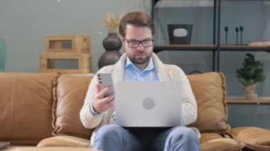 Orta yaşlı adam telefonda dizüstü bilgisayarla konuşuyor.