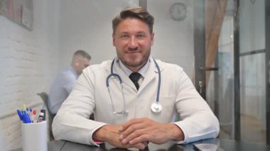 Kameraya bakan gülümseyen erkek doktorun portresi.