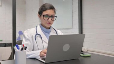 Dizüstü bilgisayar kullanırken kameraya bakan Hintli genç doktor