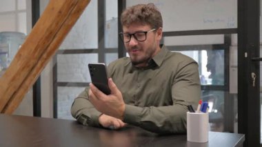 Orta yaşlı adam telefonuyla görüntülü konuşma yapıyor.