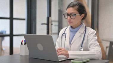 Başparmakları aşağıda kameraya bakan Hintli kadın doktor.