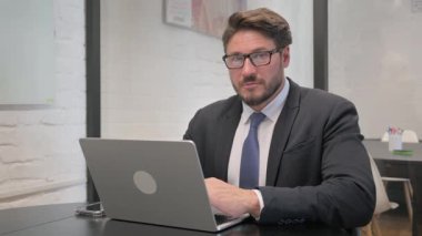 Şok olmuş Orta Çağ İşadamı Bilgisayarda çalışırken Kameraya Bakıyor