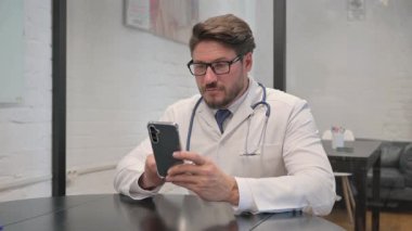 Klinikte akıllı telefon kullanan orta yaşlı bir doktor.