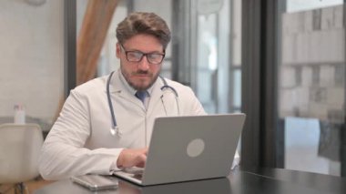 Young Doctor Typing on Laptop in Clinic