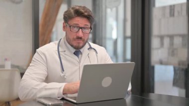 Thumbs Down by Young Doctor Working on Laptop