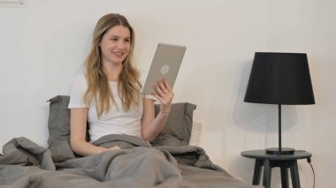 Yatakta otururken Tablette Video Sohbeti Yapan Genç Kadın