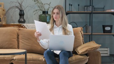 Evrak işleri yapan ve dizüstü bilgisayar kullanan genç bir kadın.