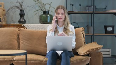 Kızgın genç kadın telefonda konuşuyor ve dizüstü bilgisayarla çalışıyor.