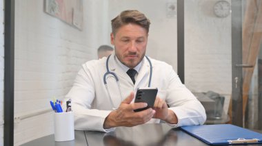 Yetişkin Doktor, hastanede akıllı telefon kullanıyor.