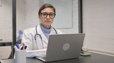 Dizüstü bilgisayar kullanırken kameraya bakan Hintli genç doktor