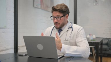 Orta yaşlı doktor video sohbetinde hastayla konuşuyor.