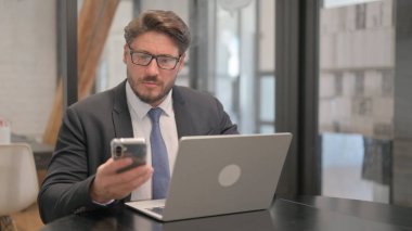 Yetişkin İş Adamı Bilgisayarda Telefon ve Daktilo Kullanıyor