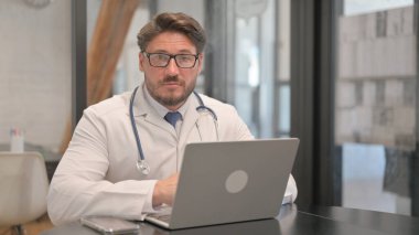Young Doctor Looking at Camera while Using Laptop