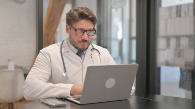Young Doctor Typing on Laptop in Clinic
