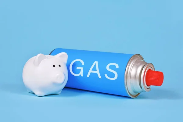 Gas cartridge bottle with piggy bank on blue background. Concept for saving gas.
