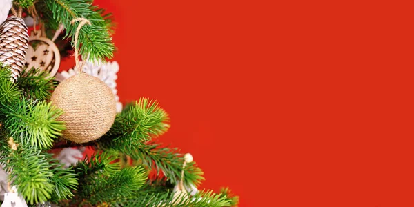 Banner with Christmas tree branches with natural ornament bauble made from beige jute rope on red background