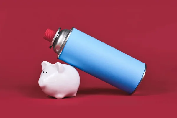 Gas cartridge bottle with piggy bank on red background. Concept for saving gas.