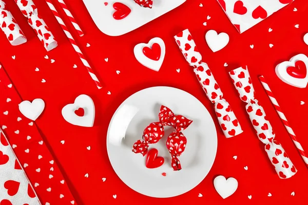 Valentine's Day decoration with candy, heart ornaments and sugar sprinkles on red background