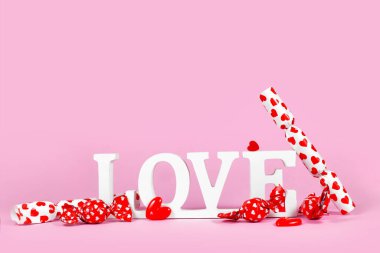 White wooden word LOVE with candy with hearts on pink background with copy space