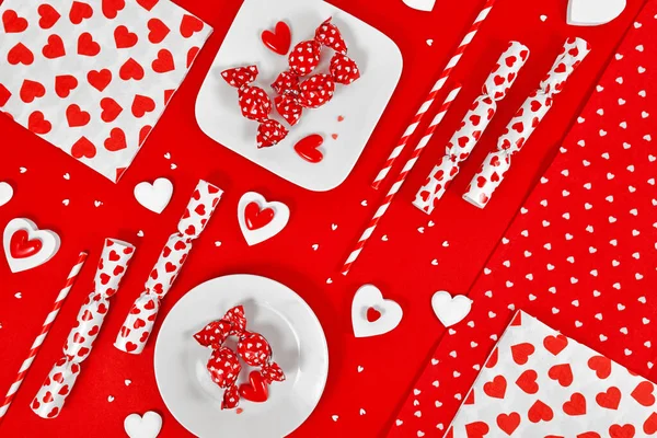 Valentine\'s Day decoration with candy, heart ornaments and sugar sprinkles on red background