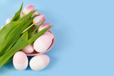 Easter decoration with painted eggs in heart shaped plate and pink tulip flowers on blue background 