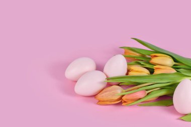 Pembe arka planda Paskalya yumurtaları olan turuncu bahar laleleri.