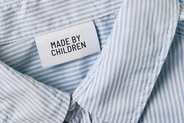 Clothing label with text saying \'Made by children\'. Child labor concept