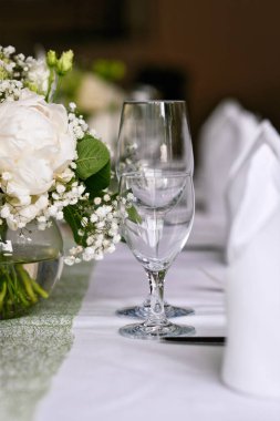Şık su ve şarap kadehleri ve beyaz çiçeklerle düğün masası.