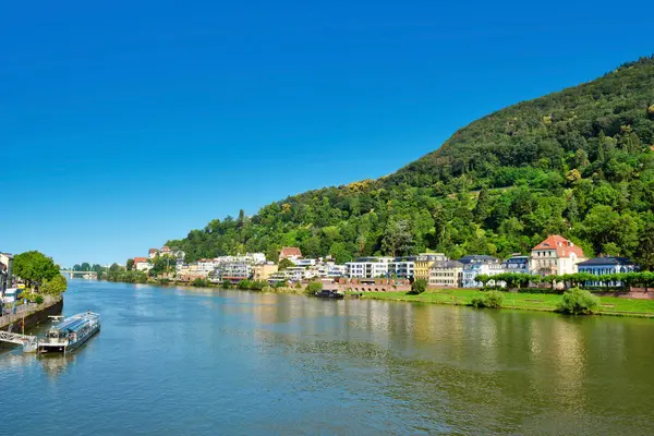 Heidelberg, Almanya - 28 Haziran 2024: Mavi gökyüzü ile yaz aylarında sokak ve konut binaları ile aşağı Neckar nehir kıyısına bakın