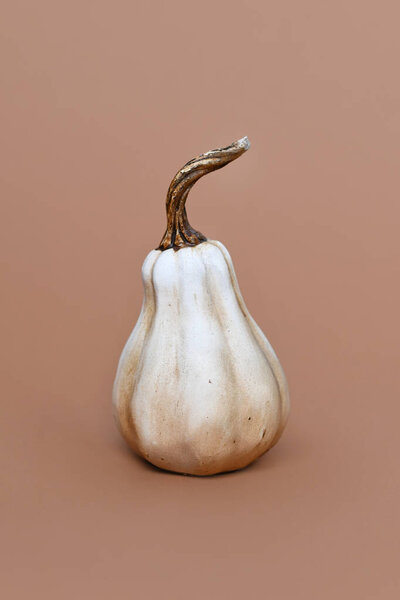 Single ceramic pumpkin ornament on brown background. Minimal autumn decoration object