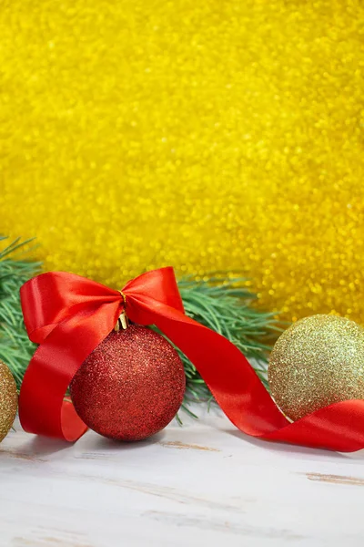 Shiny red and gold balls with bow and twisted ribbon at back of spruce branch. Yellow blurred glitter vertical background. Christmas, New Year. Copy space