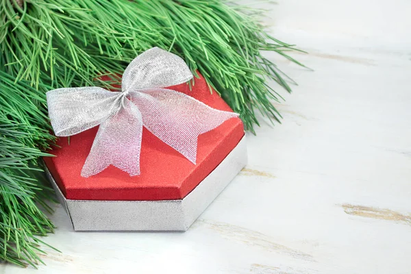 Red gift box with silver bow with spruce branches on white table. Christmas, New Year, birthday. Copy space