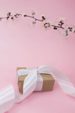 Branch of cherry, apricot, sakura with gift box with ribbon on pink background. Holidays, International women's day, Mother's day, birthday, March 8. Vertical. Copy space