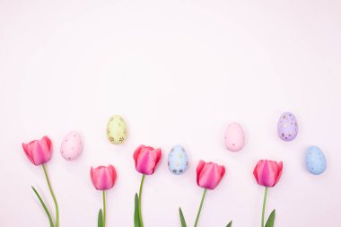 Pink tulips with painted eggs with place for text. Easter, spring. Pastel background. Copy space