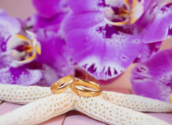 Anneaux Mariage Dorés Sur Étoile Mer Blanche Derrière Orchidées Violettes — Photo