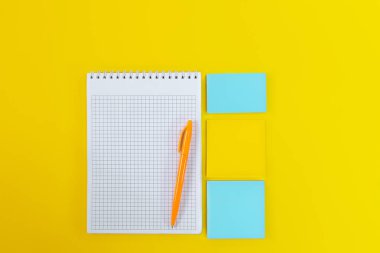 Sarı arkaplandaki renkli çıkartmaların yanında boş ve boş sayfaları olan açık defterin üst görünümü. Okula dönelim. Boşluğu kopyala