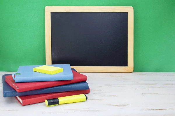 白いテーブルの上にマーカーでノートパッドのスタック 緑の背景に黒い板 学校に戻る スペースのコピー — ストック写真