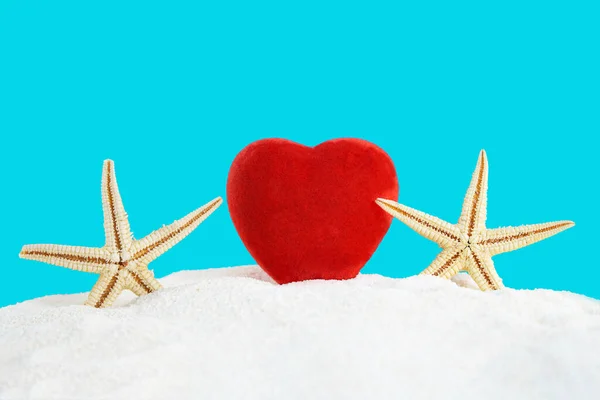 Red heart with sea stars on the sand of the beach with the sea. Valentine\'s Day, February 14, holiday in hot countries. Copy space