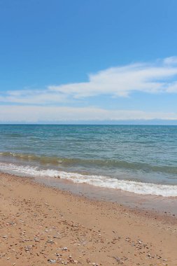 Dalgalı kumsal, mavi gökyüzünde ve dağlarda çakıl taşı olan ıslak kum. Deniz, okyanus arka planı. Tatil ve tatil macerası konsepti. Dikey