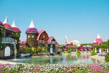 Serin gölün ve çağlayan şelalenin zemininde sergilenen çarpıcı petunya manzarası. Kaleler, binalar, uçaklar çiçeklerden yapılmıştır. Bahçıvanlık, doğa, insanlar olmadan sakin bir ortam. Doğal park