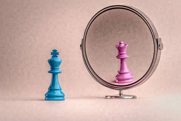 Conceptual image to represent sexual identity and gender transitioning. A blue chess king representing the male sees himself as a woman, the pink queen, in the mirror. 3D illustration.