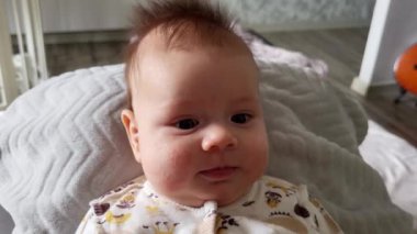 Bebek yatakta ve komik bir gülümsemesi var. Beyaz tişörtlü bebek.