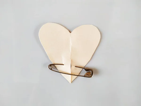 Paper heart with metal safety pin on white background, International Safety Pin Day concept