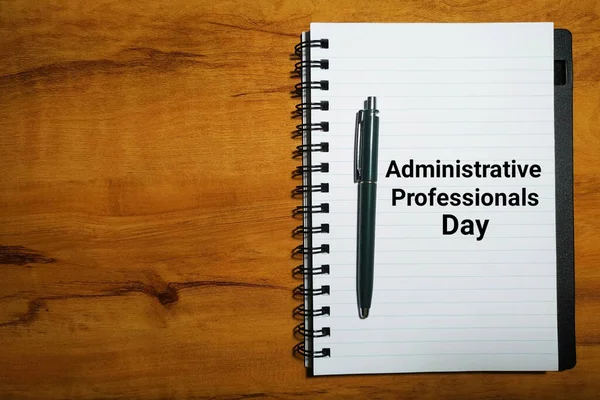 Administrative Professionals Day concept with notebook and pen on wood table background.