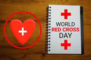 Dünya Kızılhaç Günü konsepti. Not defterinde kırmızı haç ve kalp sembolü var. Ahşap arkaplan.