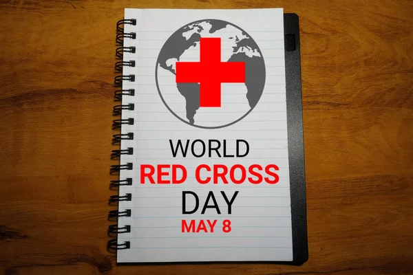 World Red Cross Day text on notebook with world map and red cross on wooden background. Suitable for greeting card, poster and banner