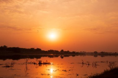 Hindistan 'da, nehrin üzerinde gün batımında, sudaki yansımayla.