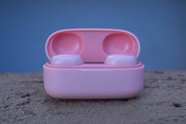 Pembe kablosuz tomurcuk davası mavi arka planda kumda.